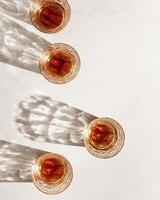 Whiskey Glasses with shadows at sunlight on beige textured background, minimal aesthetic flat lay shiny glasses, sun glare, stong alcohol drink concept, summer still life top view, copyspace photo
