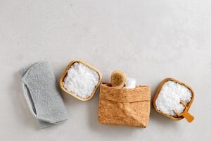 Natural wellness, bath accessories as minimal flat lay pattern, sea salt flakes in wooden bowls, soft gray towels, brush, reusable cotton pads, grey conctrete background, top view neutral colors photo