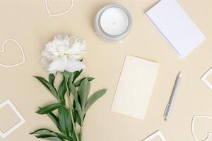 Desktop for romantic holiday with peony flower, empty paper for writing congratulations, hearts and photo, lit candle photo