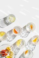 Crystal glasses with citrus slices in water on white background with rainbow reflections at sunlight, modern, minimal composition with glass cups filled with water and citrus fruit, as lemon orange photo