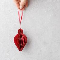 Red paper cut bauble with golden shiny shape as Lantern hanging in hand, Merry Christmas and happy New Year Seasonal winter holiday greetings card. Minimal flat lay. Top view aesthetic xmas photo