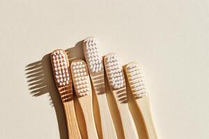 Aesthetic Beige bamboo toothbrushes with white bristles at sunlight on beige background. Simplicity, hygiene, and environmentally friendly alternatives, top view photo, minimal flatlay neutral color photo