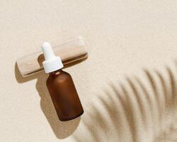 Anti aging serum with collagen and peptides in dark glass bottle with dropper on sandy background with sunlight and shadows photo