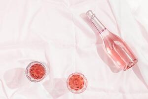 Bottle of rose champagne wine and two glasses with drink on white tablecloth. Summer vacation concept. photo