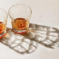 Crystal Glasses with strong drink, beautiful shadow at sunlight on beige textured background, minimal trend, aesthetic side view shiny glass, sun glare, strong alcohol drink concept, summertime, photo