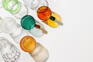 Colored Glasses pattern with sun shadow and sunlight reflection white background, minimal aesthetic top view summer still life, refraction at shine drink, caustic effect, green yellow glass cups photo