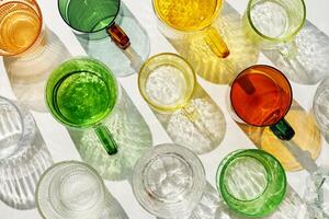 Vibrant set of colorful glass cups on white background, casting artistic light reflections and shadows in natural sunlight. Summer drink concept, minimal pattern of transparent glasses photo