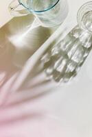 Transparent Water Glasses and water jug with palm leaf shadows at sunlight on white, pastel color photo minimal style, aesthetic top view shiny cups sparkling at natural light, summer drinks