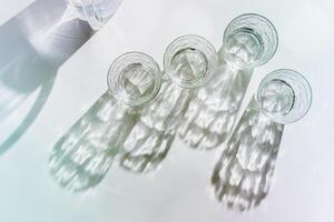 Water Glasses and water jug with Shadows and sunlight Reflection on white background, colored photo minimal style, aesthetic summer still life, refraction through crystal shine cups, caustics effect