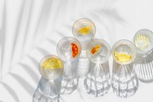 Citrus Infused Water in clear Glasses casting artistic light reflections and palm leaf shadows at sunlight. Summer drink concept, minimal pattern, flavored water with slices of fruit photo
