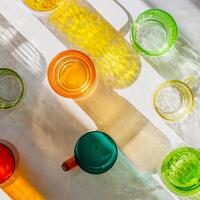 Colorful glowing glass cups on white background, casting artistic light reflections and shadows in natural sunlight. Summer drink concept, minimal trend pattern of transparent glasses, caustics photo