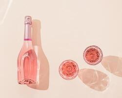 Bottle of rose champagne wine and two glasses with drink in bright sunlight. Summer vacation concept. photo