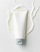 A white tube of cream with a gray cap surrounded by a splash of white cream on a white background photo