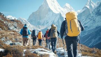 A group of hikers traverses a mountain trail under clear skies, surrounded by snow-capped peaks photo