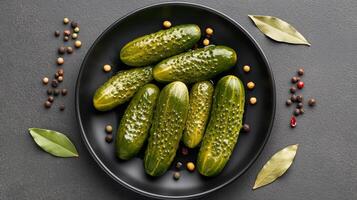 Whole pickled cucumbers glisten with brine and sit surrounded by spices on a dark plate, ideal for snacking photo