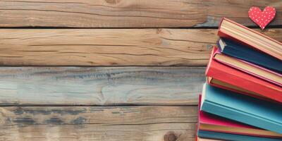 A stack of colorful books on a wooden background with a red heart on top photo