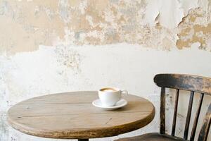 A round wooden table holds an untouched coffee cup beside a single chair in a forgotten cafe photo