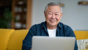 Senior asian man working on laptop in cozy living room relaxed environment home setting photo