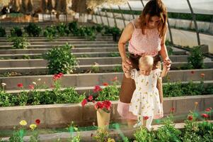 Baby is standing. Mother and daughter are in the greenhouse photo