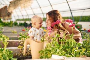 Showing red flowers to the baby. Mother and daughter are in ,,the greenhouse.. photo