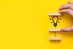 A creative idea represented by a hand arranging wooden blocks with a drawn lightbulb on a bright yellow background photo