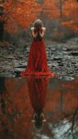Woman in red dress stands by reflective water in autumn forest, expressing deep emotion amid vibrant foliage photo