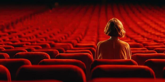 Person sits alone in empty theater with red seats during a quiet moment of reflection photo