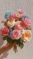 Beautiful bouquet of colorful flowers held against a textured wall on a sunny day photo