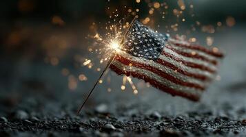 Fireworks spark from a small American flag on a gravel surface during a nighttime celebration photo