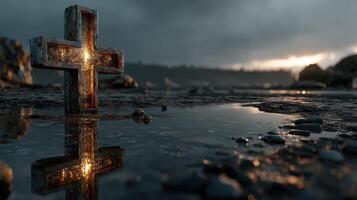 Cross reflecting in water at dusk near a rocky shoreline with dramatic clouds and soft glimmers of light photo