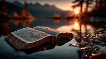 Book resting on wet stones at sunrise near calm water surrounded by mountains photo