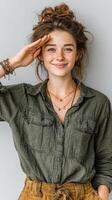 Young woman with freckled skin and a playful smile saluting against a simple gray background photo