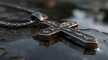 Detailed silver cross necklace rests on a reflective surface surrounded by droplets at dusk photo