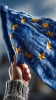 Person holds European Union flag against cloudy sky, showcasing unity and support for Europe during a public rally photo