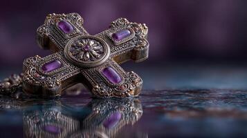 Silver ornate cross with purple gemstones rests on a reflective surface during evening light photo