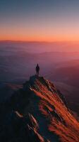 Hiker stands on mountain peak at sunset overlooking vast valleys and distant hills photo