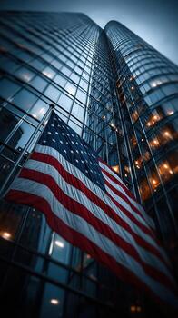 Flag waving in front of a tall glass building during twilight in an urban setting photo