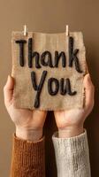 Hands holding a thank you sign made of black rope against a neutral background photo
