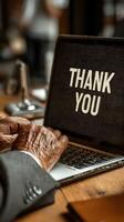 Thank you message displayed on laptop screen as hands type on keyboard in a warm office setting photo