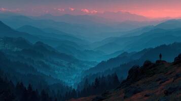Sunset over mountain range with silhouette of a person standing on a rocky outcrop photo