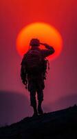 Soldier saluting the sunset with a warm red backdrop overlooking a mountainous landscape photo