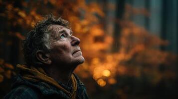 Elderly man gazing upward in a forest with warm autumn foliage illuminated by a faint glow in the early evening photo