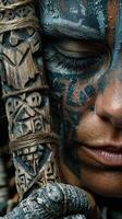 Close-up of a person with intricate face paint holding a carved wooden staff in a nature setting during the day photo