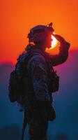 Soldier silhouetted against a vibrant sunset while saluting in a mountainous environment photo