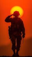 Soldier salutes the setting sun in a dramatic silhouette against a vibrant orange sky photo