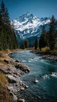 Snow-capped mountain peaks reflect in a clear river surrounded by evergreen trees in a serene landscape photo