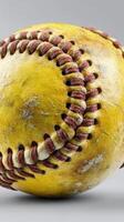 Weathered yellow softball with red stitching lying on a neutral background photo