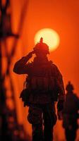 Soldier salutes during sunset, silhouetted against vibrant orange sky in a military operation photo