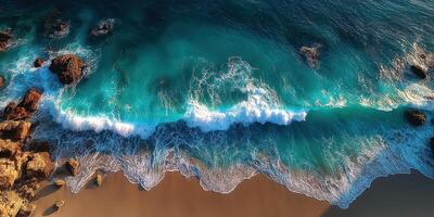 Waves crashing onto golden sandy beach with rocky formations under bright sunlight photo