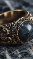 Intricate antique bracelet featuring dark stone set in detailed gold filigree on textured surface photo